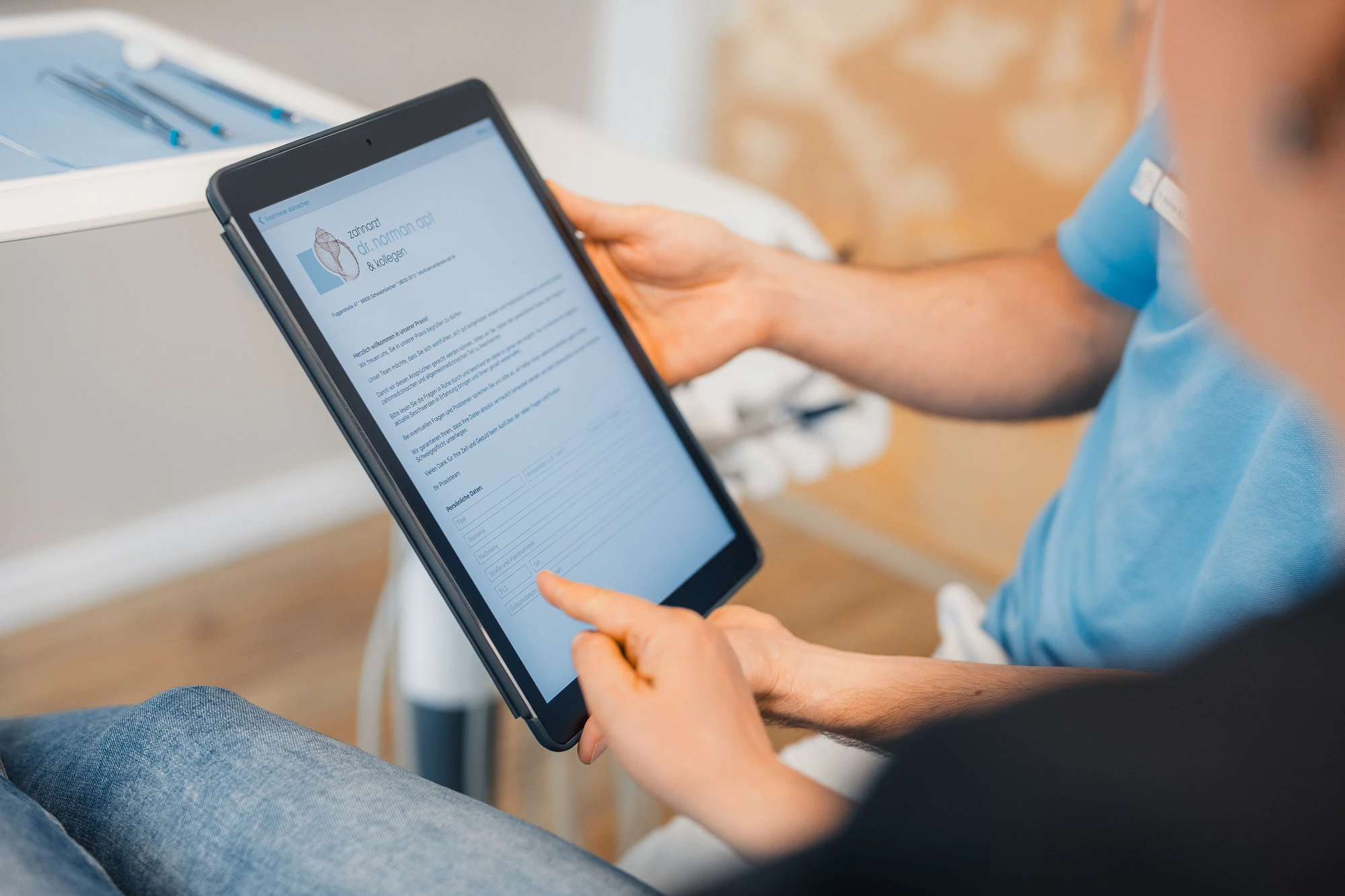 Detailaufnahme: Ein Mitarbeiter des Zahnzentrums Schwabmünchen zeigt einem Kunden auf einem Tablet ein Kontaktformular der Praxis